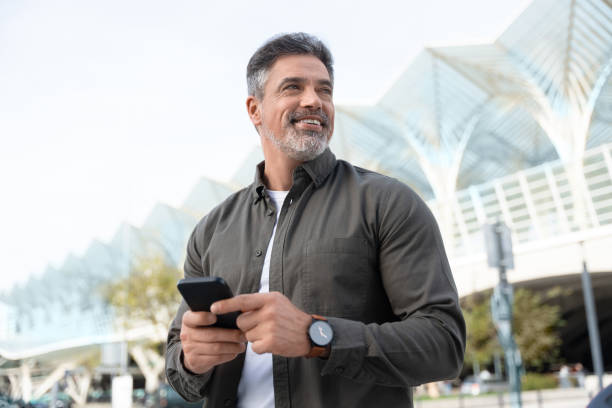 Indian or latin confident middle age male entrepreneur businessman holding mobile cell phone for work. Confident mature hispanic senior business man using smartphone cellphone app at office building